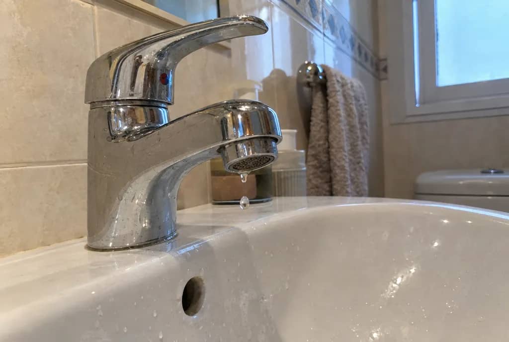 Grifo monomando cromado de lavabo con una gota colgando del aireador y otra cayendo al lavabo